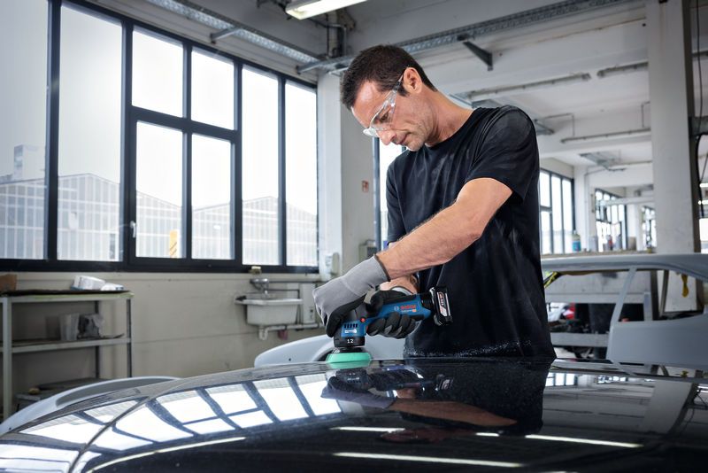 บุคคลที่สวมอุปกรณ์ความปลอดภัยกำลังขัดฝากระโปรงรถยนต์ในอู่ซ่อมรถยนต์.