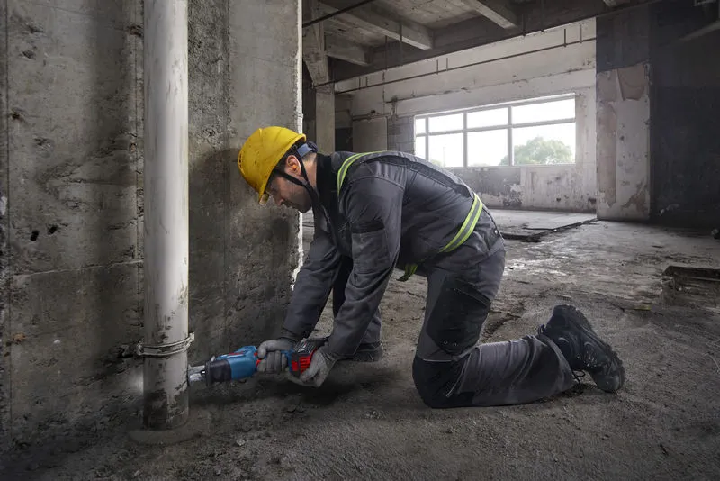 บุคคลที่สวมอุปกรณ์ด้านความปลอดภัยใช้เลื่อยตัดท่อบริเวณใกล้กับกำแพงคอนกรีต.