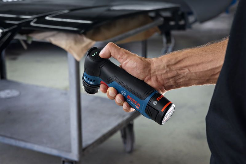 คนๆ หนึ่งถือเครื่องขัดแบบสั่นสะเทือนแบบไร้สายไว้ใกล้โต๊ะทำงานโลหะ.