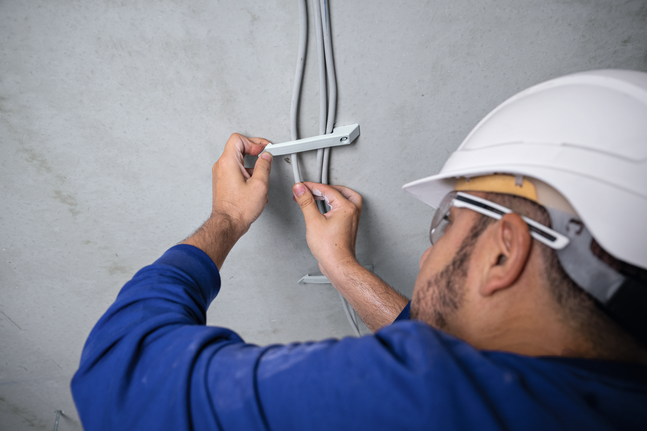 บุคคลที่สวมอุปกรณ์ด้านความปลอดภัยติดตั้งตัวยึดสายเคเบิลบนเพดาน.