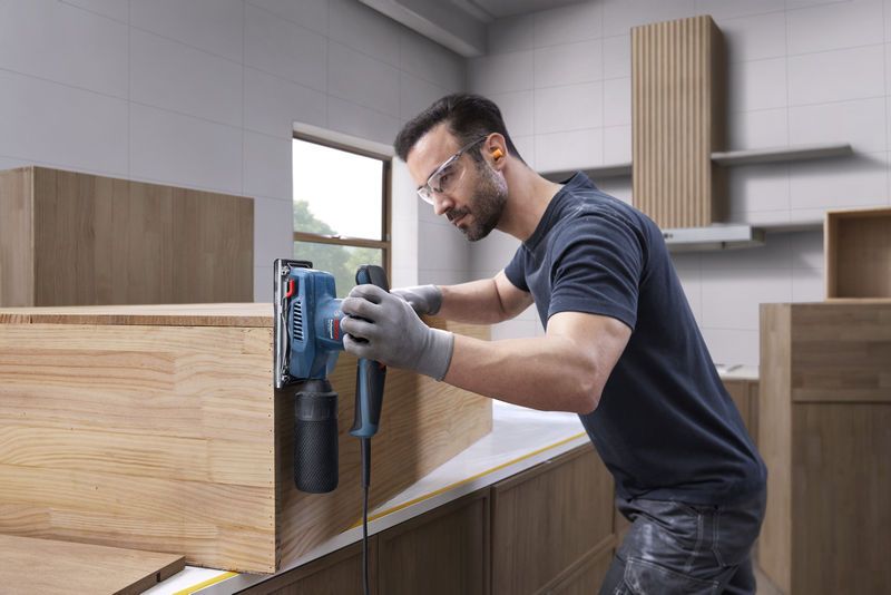 บุคคลที่สวมอุปกรณ์ด้านความปลอดภัยกำลังขัดตู้ไม้โดยใช้เครื่องขัดแบบสั่น.