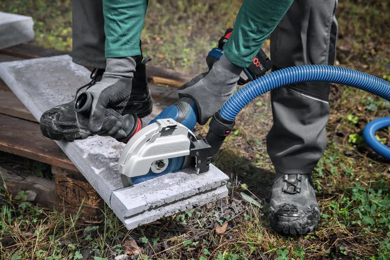 บุคคลที่สวมอุปกรณ์ด้านความปลอดภัยใช้เครื่องเจียรขนาดใหญ่พร้อมเครื่องดูดฝุ่นเพื่อตัดคอนกรีต.