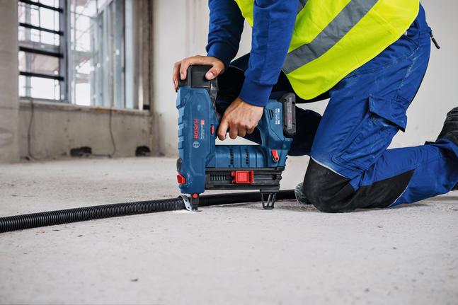 บุคคลที่สวมอุปกรณ์ด้านความปลอดภัยใช้ปืนยิงตะปูไร้สายเพื่อยึดท่อร้อยสายบนพื้นคอนกรีต.