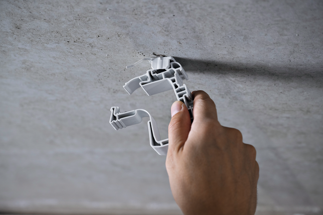 คนๆ หนึ่งกำลังติดตั้งตัวยึดพลาสติกบนเพดานคอนกรีต.