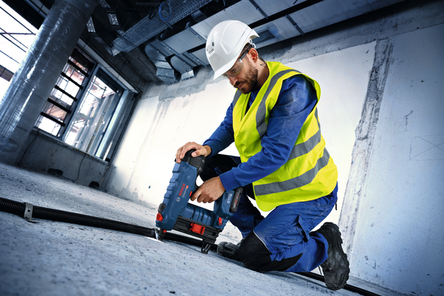 บุคคลที่สวมอุปกรณ์ด้านความปลอดภัยใช้เครื่องมือไฟฟ้าเจาะลงไปในพื้นคอนกรีต.