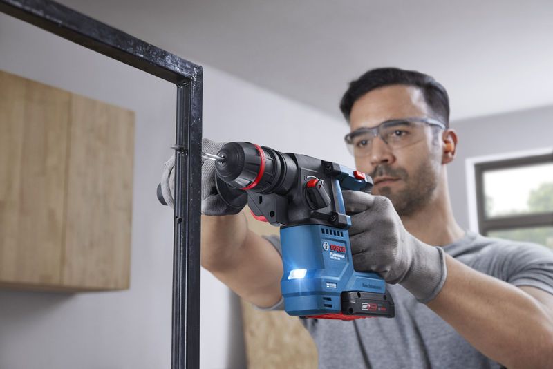 บุคคลที่สวมอุปกรณ์ด้านความปลอดภัยกำลังเจาะเข้าไปในโครงโลหะโดยใช้สว่านโรตารี่ไร้สาย.