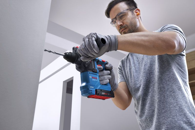 บุคคลที่สวมอุปกรณ์ด้านความปลอดภัยกำลังเจาะเข้าไปในผนังด้วยค้อนโรตารี่.