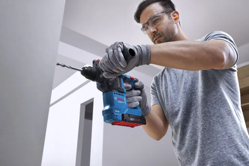 บุคคลที่สวมอุปกรณ์ด้านความปลอดภัยกำลังเจาะเข้าไปในผนังด้วยค้อนโรตารี่.