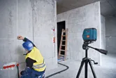 บุคคลที่สวมอุปกรณ์ด้านความปลอดภัยทำเครื่องหมายผนังโดยใช้เครื่องมือวัดระดับเลเซอร์.