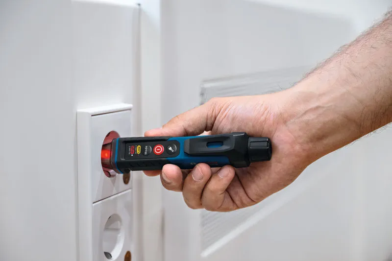 บุคคลใช้เครื่องทดสอบแรงดันไฟฟ้าแบบไม่สัมผัสใกล้กับปลั๊กไฟ.