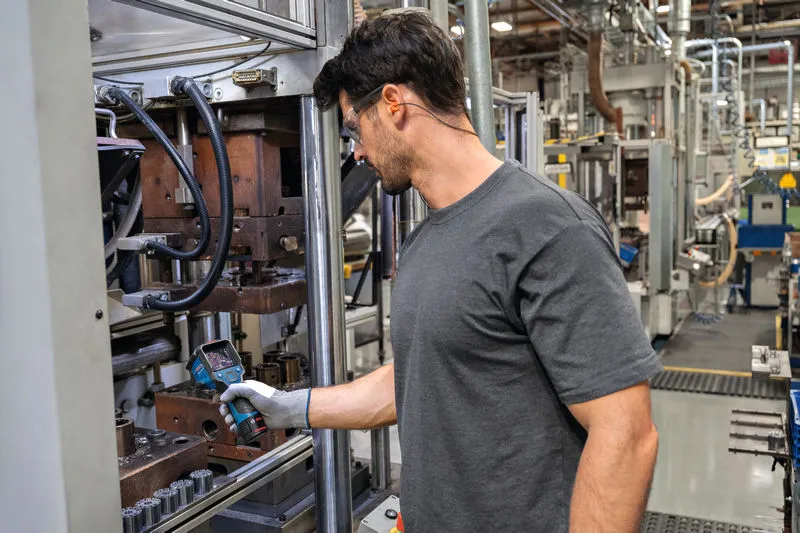 บุคคลที่สวมอุปกรณ์ความปลอดภัยกำลังตรวจสอบเครื่องจักรด้วยกล้องเทอร์โมในโรงงาน.