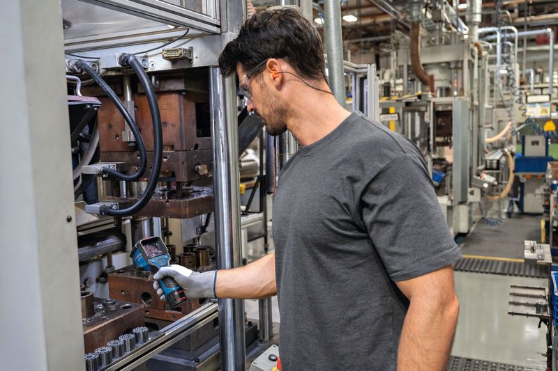 บุคคลที่สวมอุปกรณ์ความปลอดภัยกำลังตรวจสอบเครื่องจักรด้วยกล้องเทอร์โมในโรงงาน.