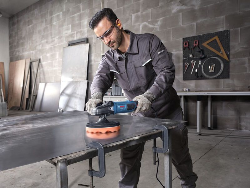 บุคคลที่สวมอุปกรณ์ด้านความปลอดภัยกำลังขัดแผ่นโลหะด้วยเครื่องมือไฟฟ้า.