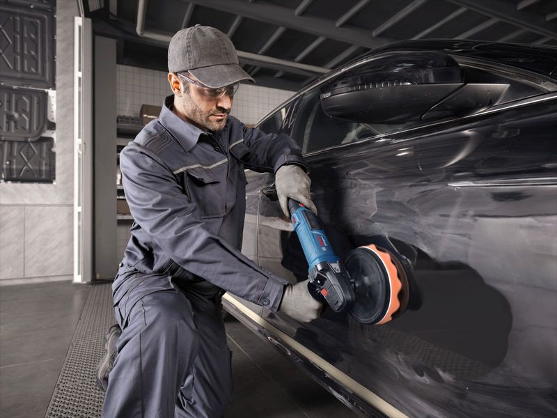 บุคคลที่สวมอุปกรณ์ความปลอดภัยกำลังขัดรถสีดำโดยใช้เครื่องมือไฟฟ้า.