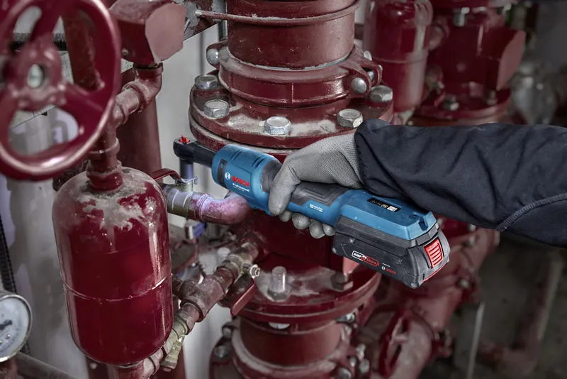 บุคคลที่สวมอุปกรณ์ด้านความปลอดภัยใช้ประแจขันแบบไร้สายกับท่ออุตสาหกรรม.