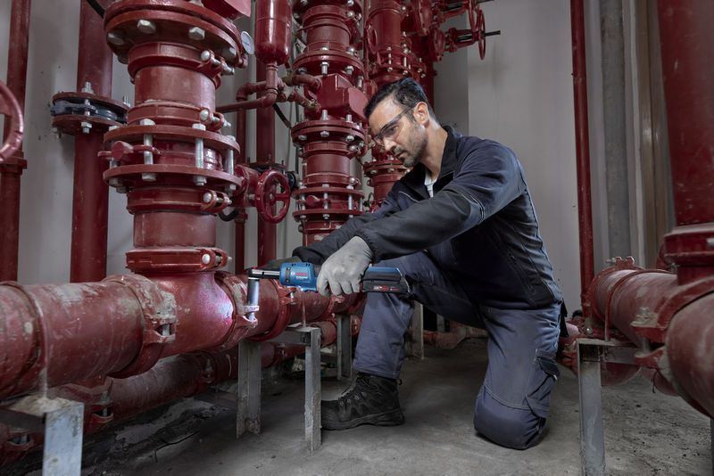 บุคคลที่สวมอุปกรณ์ด้านความปลอดภัยใช้ประแจขันไร้สายบนระบบท่อสีแดง.