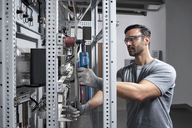 บุคคลที่สวมอุปกรณ์ด้านความปลอดภัยใช้ประแจขันแบบไร้สายบนชั้นวางโลหะ.