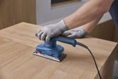 ผู้ที่สวมอุปกรณ์ด้านความปลอดภัยใช้เครื่องขัดกระดาษทรายแบบสั่นสะเทือนบนพื้นผิวไม้.