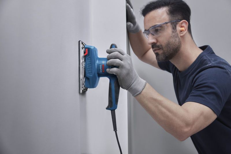 บุคคลที่สวมอุปกรณ์ด้านความปลอดภัยกำลังขัดผนังด้วยเครื่องขัดแบบวงโคจร.