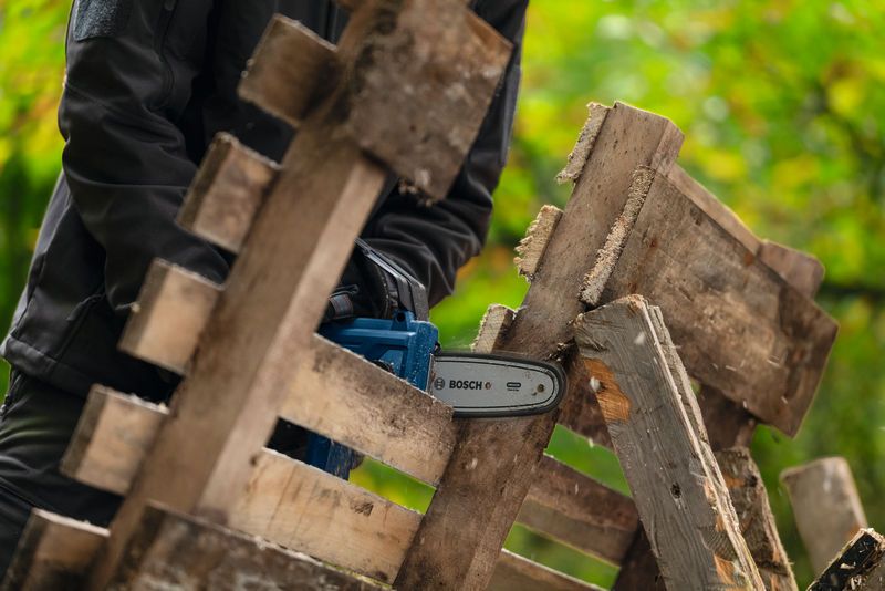 บุคคลที่สวมอุปกรณ์ความปลอดภัยกำลังตัดไม้กระดานโดยใช้เลื่อยตัดแต่งกิ่งไม้แบบไร้สาย.