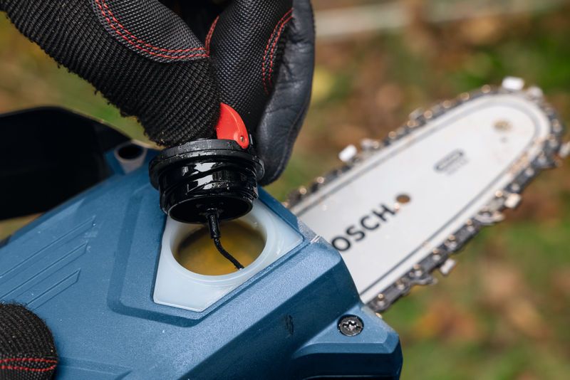 บุคคลที่สวมอุปกรณ์ความปลอดภัยเปิดฝาถังน้ำมันใกล้กับใบเลื่อยตัดแต่งกิ่งไม้แบบไร้สาย.