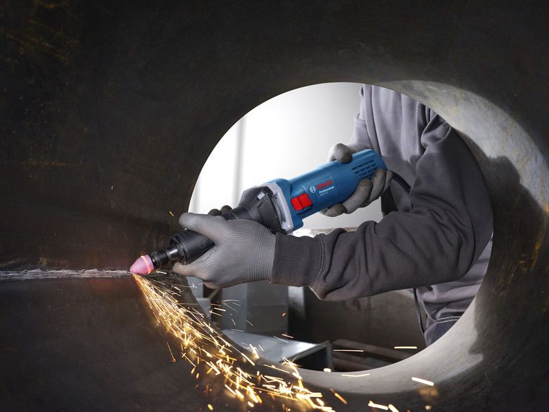 บุคคลที่สวมอุปกรณ์ด้านความปลอดภัยใช้เครื่องเจียรตรงเพื่อทำให้ภายในท่อโลหะเรียบ.