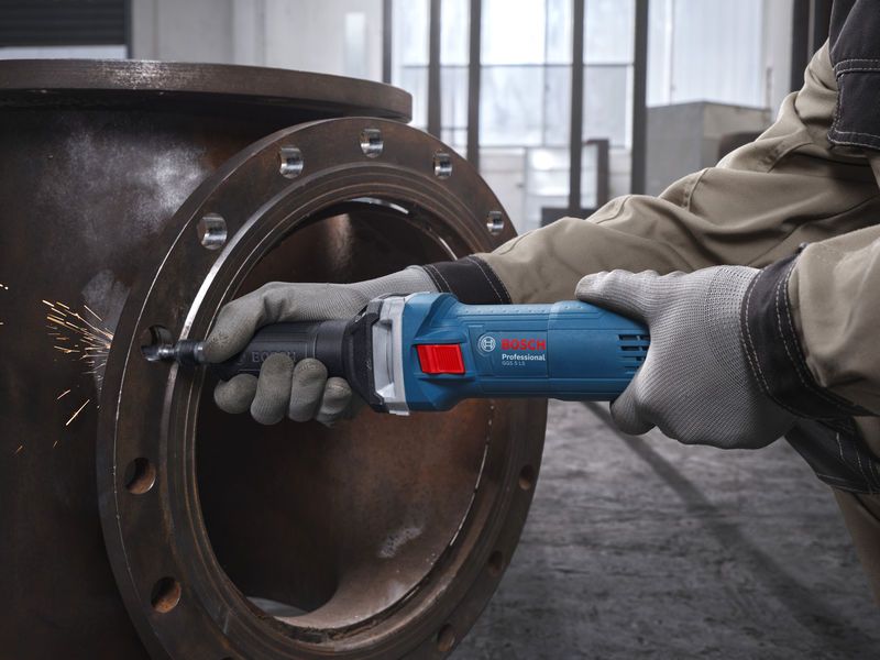 บุคคลที่สวมอุปกรณ์ความปลอดภัยกำลังเจียรท่อโลหะด้วยเครื่องเจียรตรง.