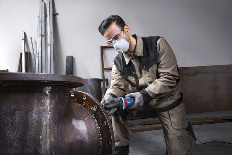 บุคคลที่สวมอุปกรณ์ความปลอดภัยกำลังเจียรขอบท่อโลหะขนาดใหญ่.