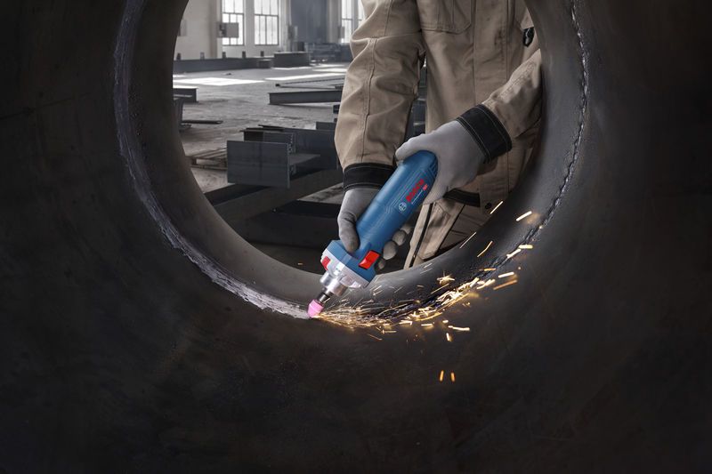 บุคคลที่สวมอุปกรณ์ด้านความปลอดภัยกำลังเจียรภายในท่อโลหะขนาดใหญ่ด้วยเครื่องเจียรตรง.