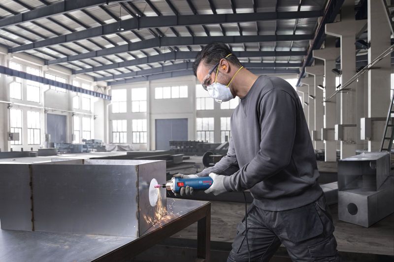 บุคคลที่สวมอุปกรณ์ความปลอดภัยใช้เครื่องเจียรตรงเพื่อเจียรกล่องโลหะ.