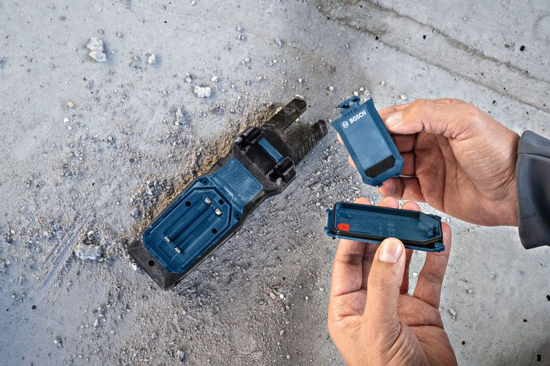 คนกำลังเปลี่ยนแบตเตอรี่ในฐานเครื่องมือไฟฟ้าบนพื้นคอนกรีตที่เต็มไปด้วยฝุ่น.