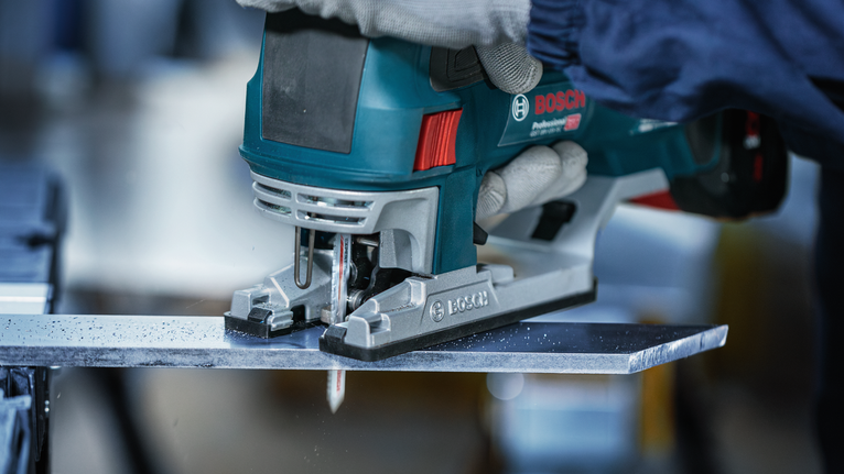 บุคคลที่สวมอุปกรณ์ความปลอดภัยกำลังตัดแผ่นโลหะโดยใช้จิ๊กซอว์มือถือ