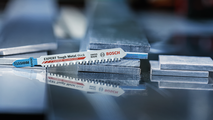 ใบเลื่อยจิ๊กซอว์วางอยู่บนแผ่นโลหะที่วางซ้อนกันบนพื้นผิวสะท้อนแสง