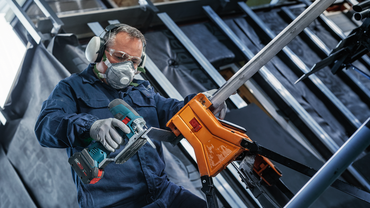 บุคคลที่สวมอุปกรณ์ความปลอดภัยตัดท่อโลหะด้วยเครื่องมือไฟฟ้าไร้สาย