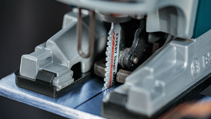 ภาพระยะใกล้ของใบเลื่อยจิ๊กซอว์ที่กำลังตัดผ่านแผ่นโลหะ