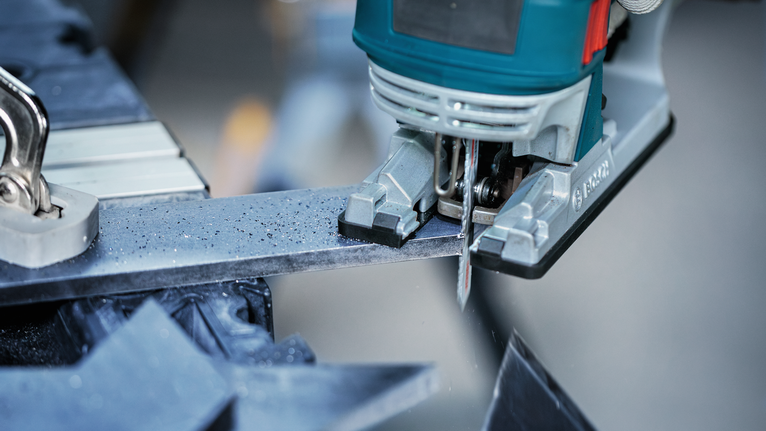 จิ๊กซอว์ตัดผ่านแท่งเหล็กในโรงงาน