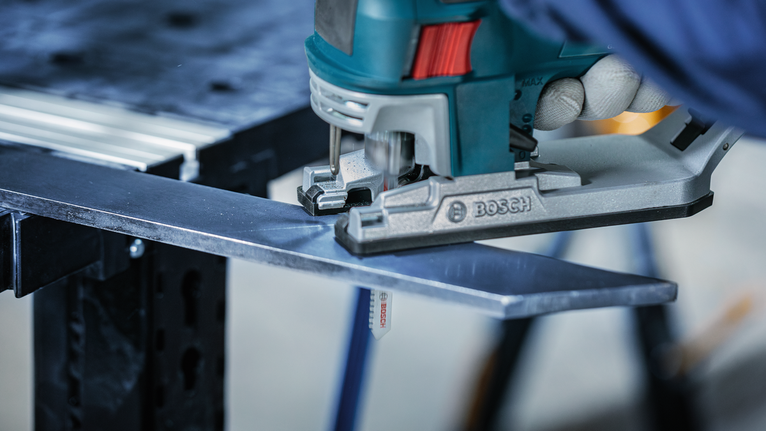 บุคคลที่สวมอุปกรณ์ความปลอดภัยกำลังตัดแผ่นโลหะด้วยจิ๊กซอว์