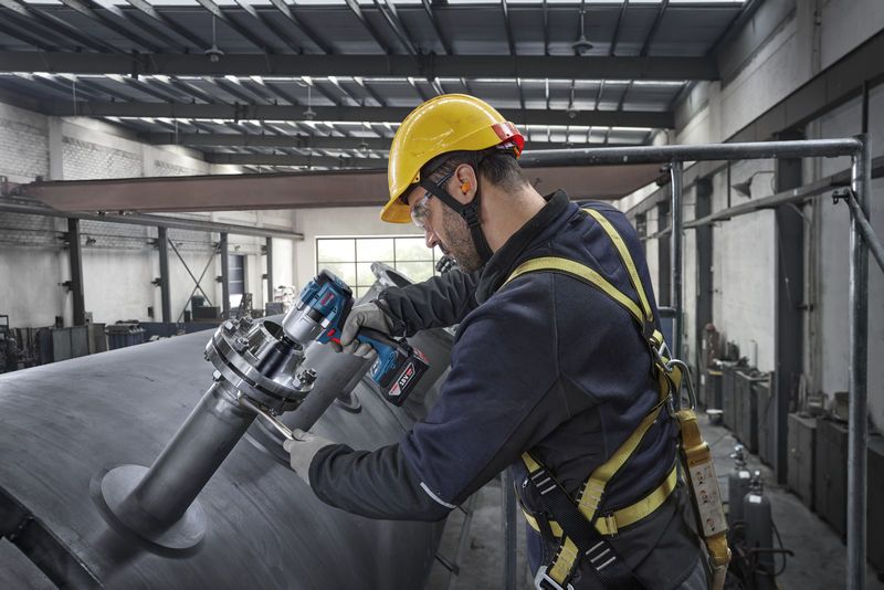 บุคคลที่สวมอุปกรณ์ด้านความปลอดภัยใช้ประแจกระแทกเพื่อขันสลักเกลียวบนถังโลหะขนาดใหญ่.