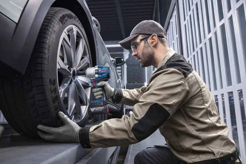 บุคคลที่สวมอุปกรณ์ด้านความปลอดภัยใช้ประแจกระแทกไร้สายเพื่อขันล้อรถยนต์.