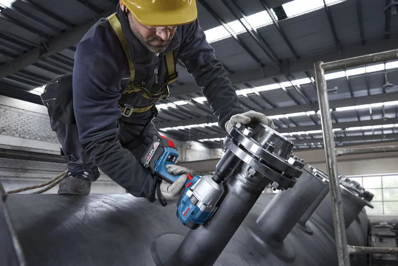 บุคคลที่สวมอุปกรณ์ด้านความปลอดภัยใช้ประแจกระแทกไร้สายกับท่ออุตสาหกรรม.