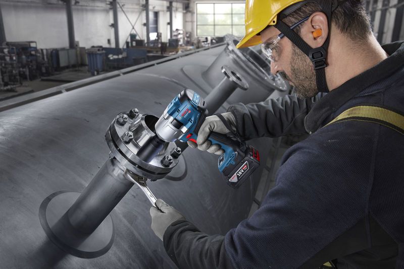 บุคคลที่สวมอุปกรณ์ด้านความปลอดภัยกำลังขันน็อตบนท่ออุตสาหกรรมด้วยประแจกระแทกไร้สาย.