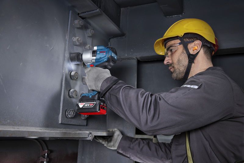 บุคคลที่สวมอุปกรณ์ด้านความปลอดภัยกำลังขันสลักเกลียวบนคานเหล็กโดยใช้ประแจกระแทกไร้สาย.