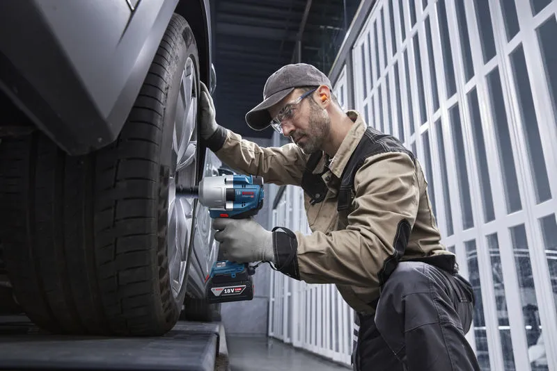 บุคคลที่สวมอุปกรณ์ด้านความปลอดภัยใช้ประแจกระแทกไร้สายกับล้อรถยนต์.