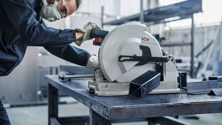 คนงานสวมอุปกรณ์ความปลอดภัยกำลังตัดคานโลหะด้วยเลื่อยวงเดือน.