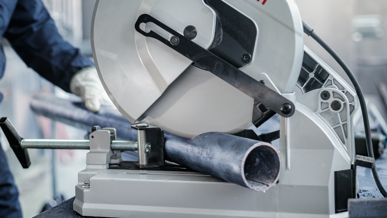 บุคคลที่สวมอุปกรณ์ความปลอดภัยกำลังตัดท่อโลหะด้วยเลื่อยนิ่ง