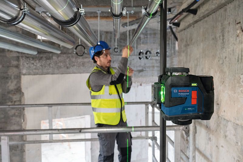 บุคคลที่สวมอุปกรณ์ด้านความปลอดภัยกำลังจัดแนวท่อโดยใช้เครื่องมือปรับระดับเลเซอร์.