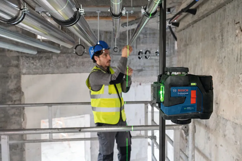 บุคคลที่สวมอุปกรณ์ด้านความปลอดภัยกำลังจัดแนวท่อโดยใช้เครื่องมือปรับระดับเลเซอร์.