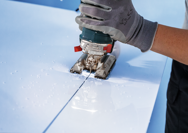 คนงานที่สวมอุปกรณ์ความปลอดภัยใช้จิ๊กซอว์ตัดเป็นเส้นตรงในแผงสีขาว.