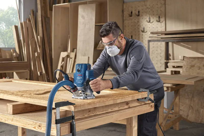 ผู้ที่สวมอุปกรณ์ป้องกันความปลอดภัยใช้เราเตอร์เพื่อขึ้นรูปไม้ในโรงงาน.