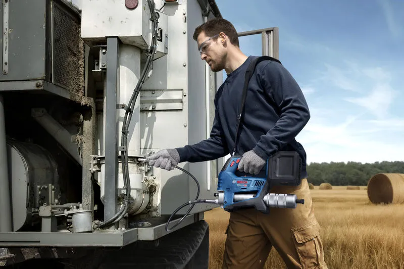 บุคคลที่สวมอุปกรณ์ด้านความปลอดภัยใช้ปืนจารบีไร้สายในการซ่อมบำรุงเครื่องจักรกลทางการเกษตร.